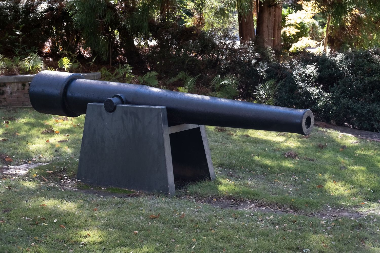 Large black naval cannon mounted on display in a garden setting.