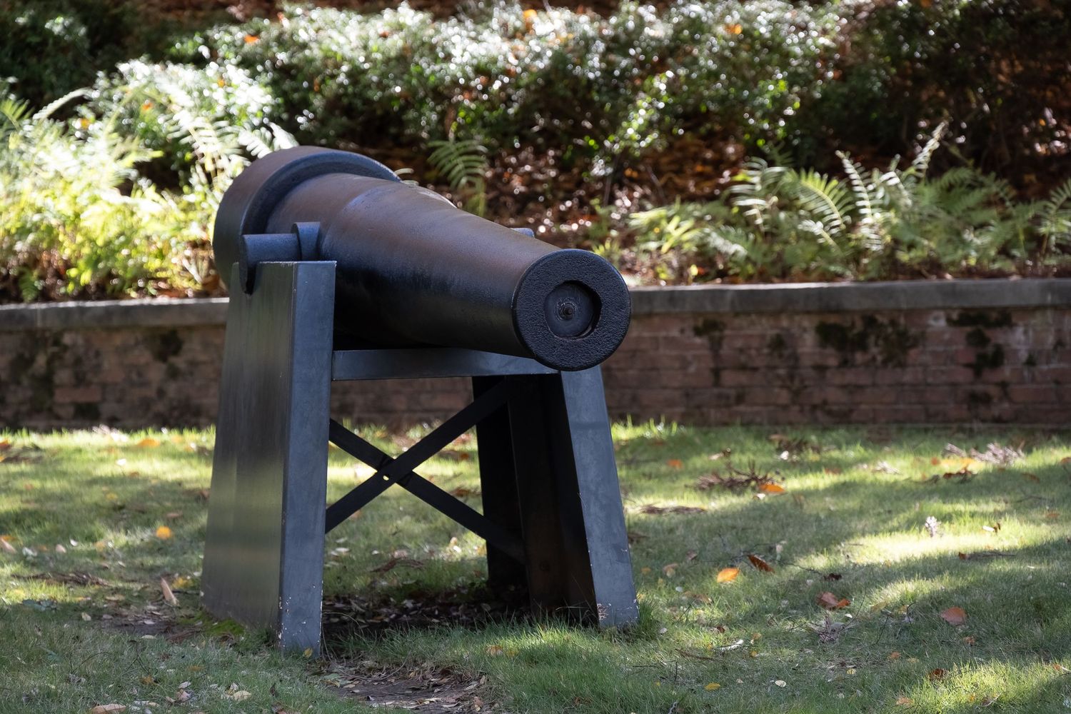An old cannon mounted on a wooden stand sits in a garden setting.