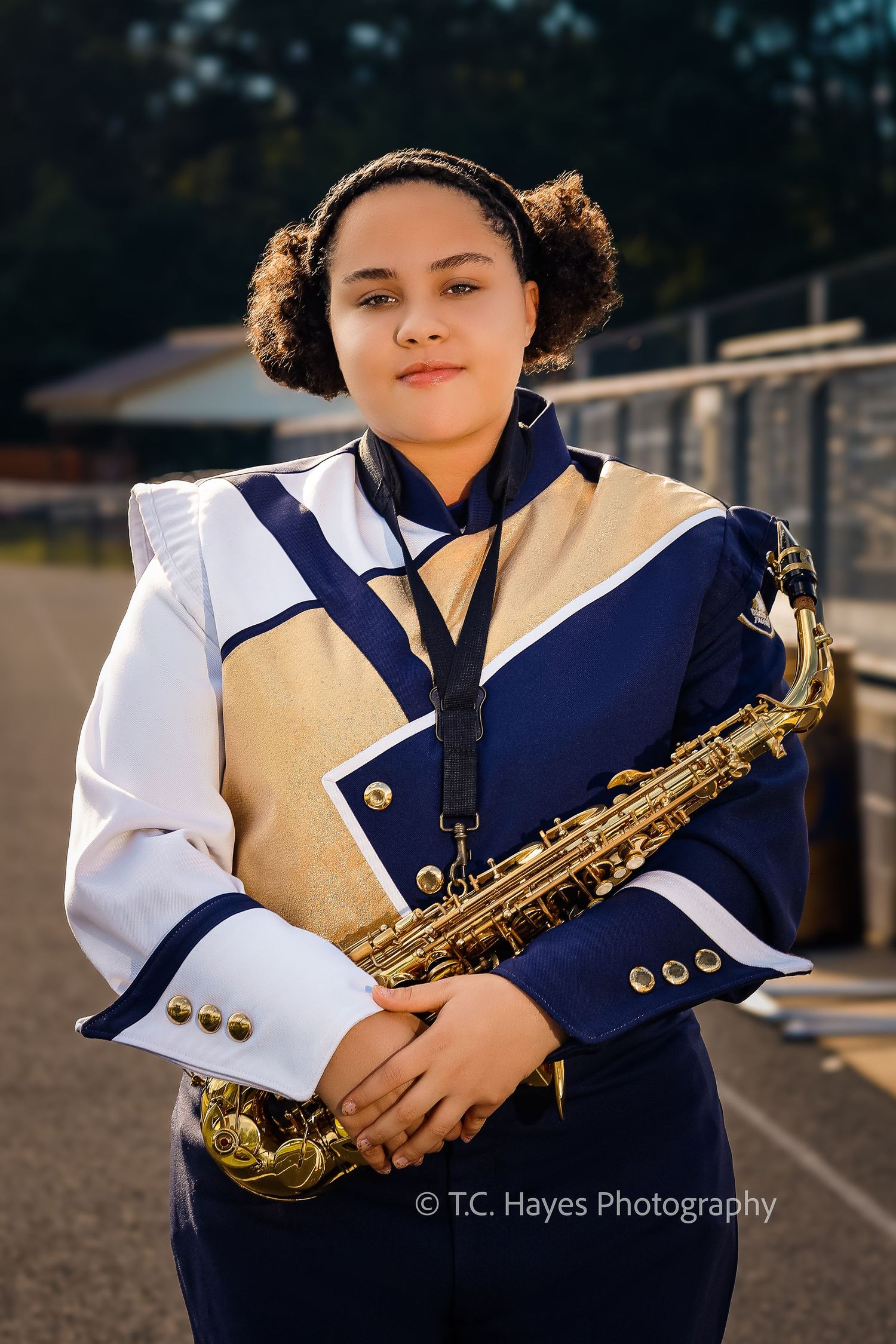 Marching band member in navy and white uniform holds a brass saxophone while posing outdoors for a portrait.