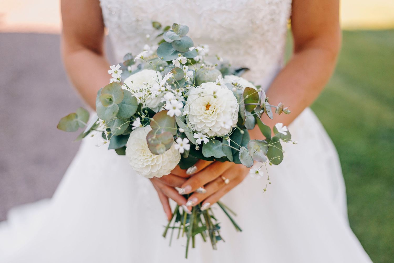A pair of white sneakers peeks out beneath layers of tulle from a wedding dress on a gravel surface.
