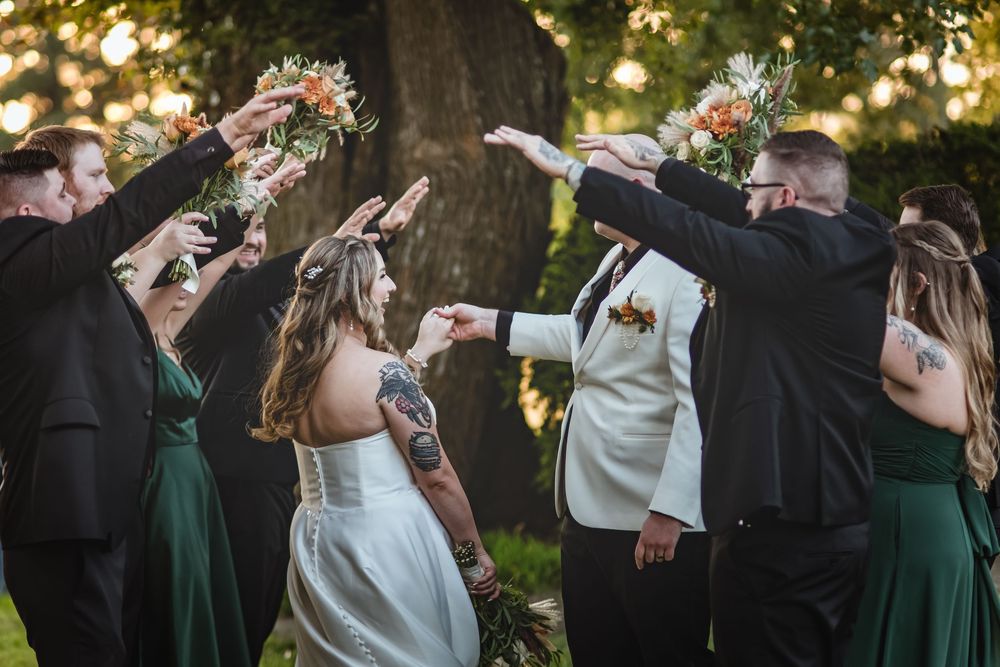 Wedding party gathered outdoors raises drinks in celebratory toast with emerald green bridesmaid dresses visible.