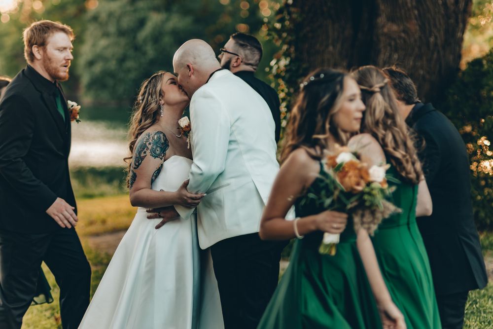 Wedding ceremony outdoors in a natural setting with bridesmaids in emerald green dresses during golden hour.