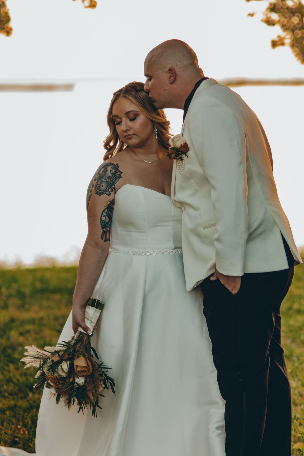 Intimate wedding moment between newlyweds during golden hour sunset with bride holding autumn-toned bouquet.
