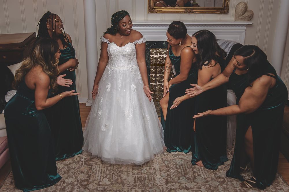 Bridesmaids in black dresses help adjust a wedding gown in an elegant room.