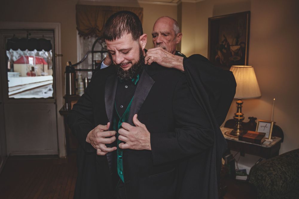 Two people having a tender interaction while wearing dark clothing and a patterned scarf indoors.
