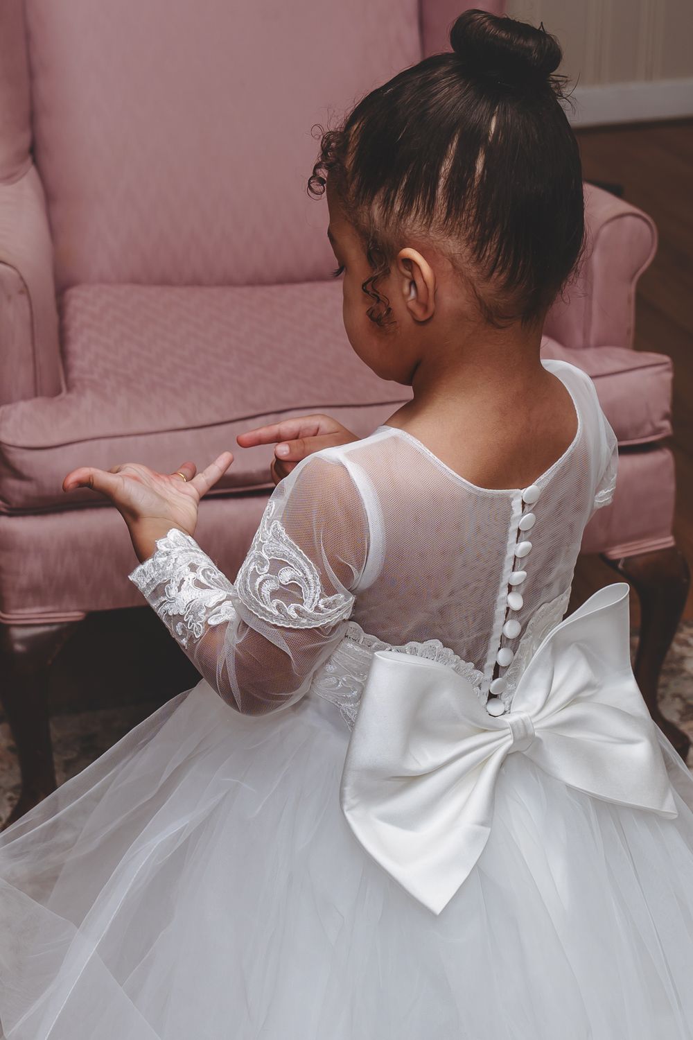 Back view of white lace flower girl dress with sheer sleeves and large bow detail.