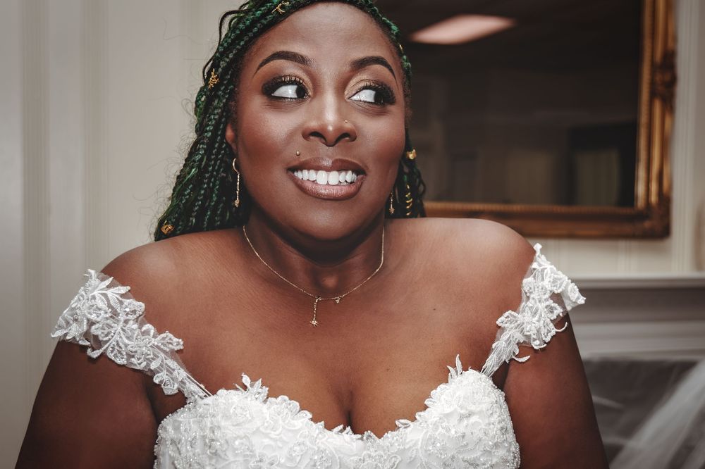 A joyful bride wearing a white lace off-shoulder wedding dress smiles radiantly.
