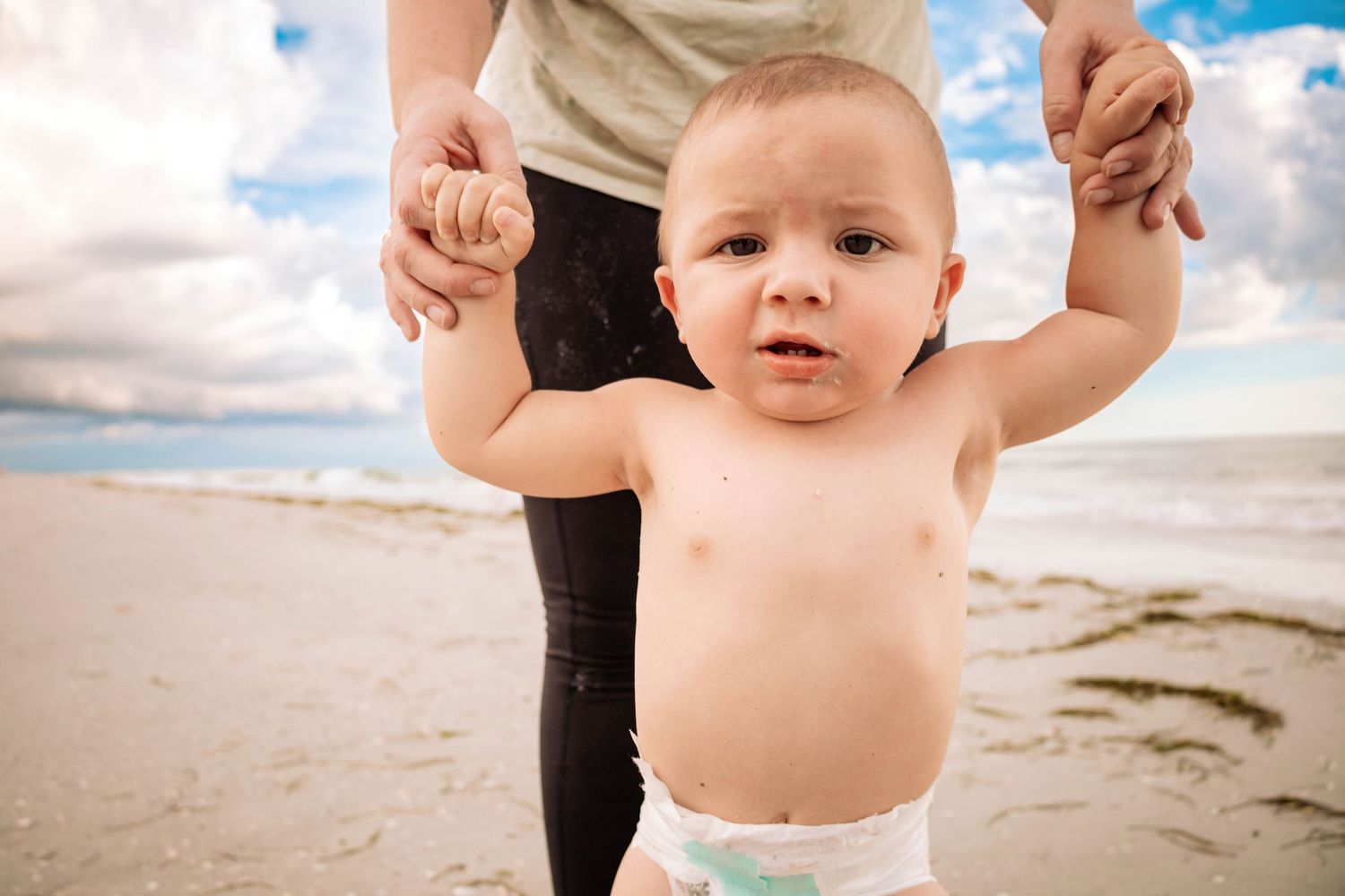 Small child's tiny feet on sandy beach with ocean waves in background.