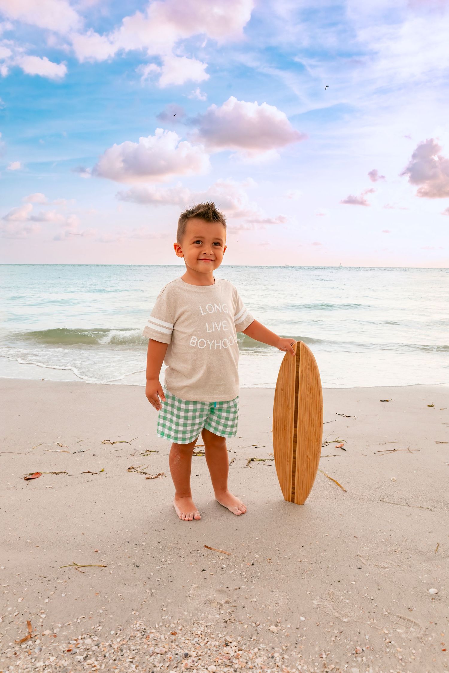 Small wooden surfboard prop sits on white sandy beach with turquoise ocean waters in background.