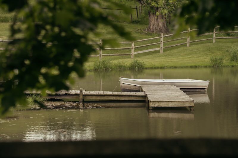 A wooden dock extends over a serene pond shady elm farms as seen from new canopied area.