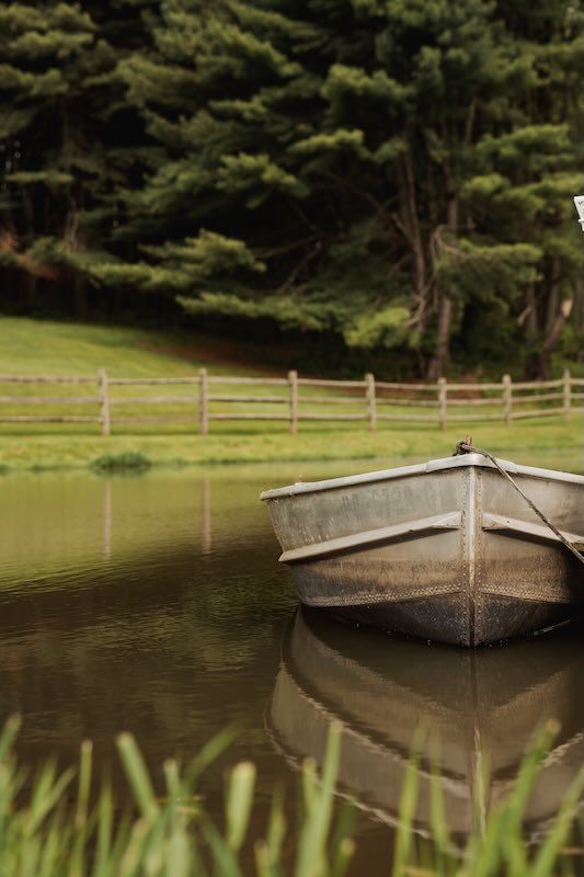 A weathered rowboat floats peacefully on a tranquil pond beside shady elm farms wedding venue ideal spot for photo & video.