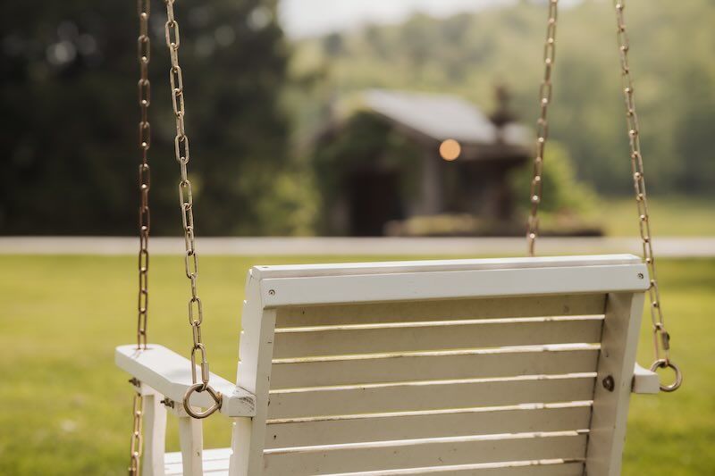 White wooden porch swing on chains against blurred green & rustic background shady elm farms wedding venue pittsburgh pa.