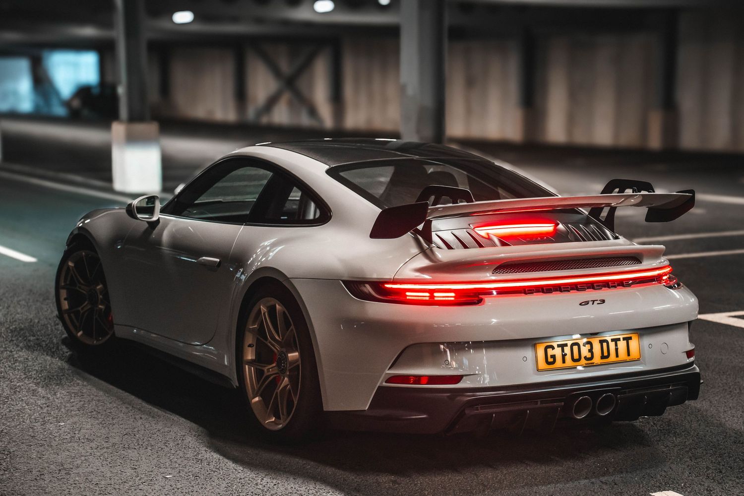 Rear view of a silver Porsche GT3 sports car with illuminated taillights parked in a dimly lit garage.