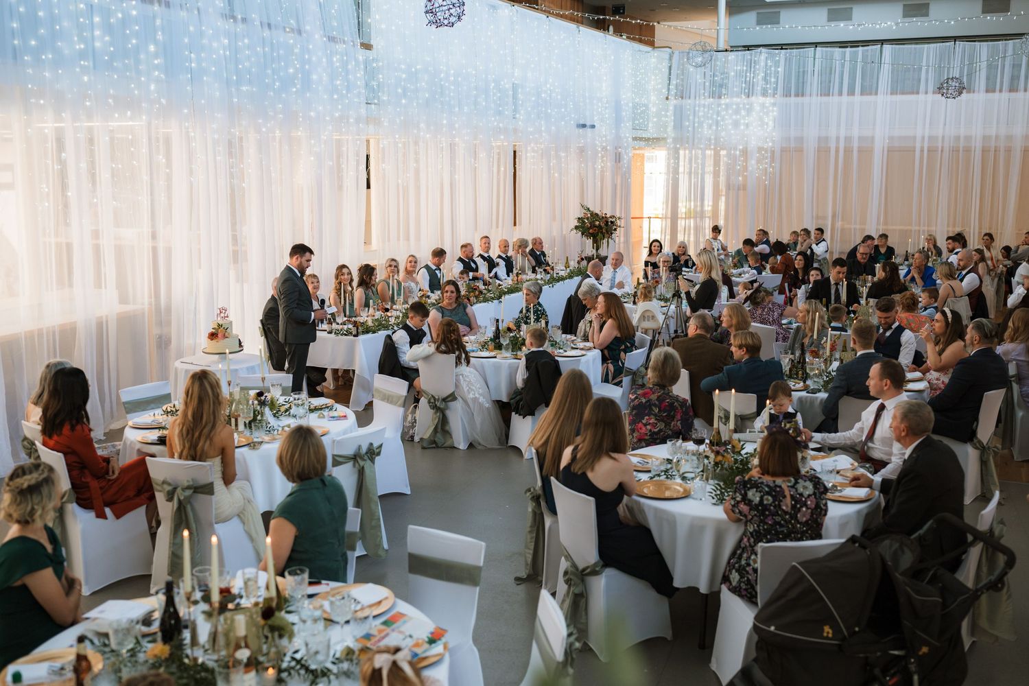 Overhead view of a formal event with round dining tables and guests seated in an elegant venue with white decor.