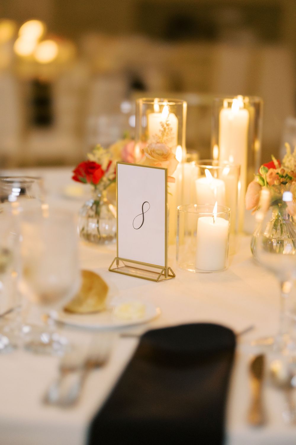 Elegant table setting with gold framed table number, glowing candles and floral centerpieces at wedding reception at Hall of Springs.