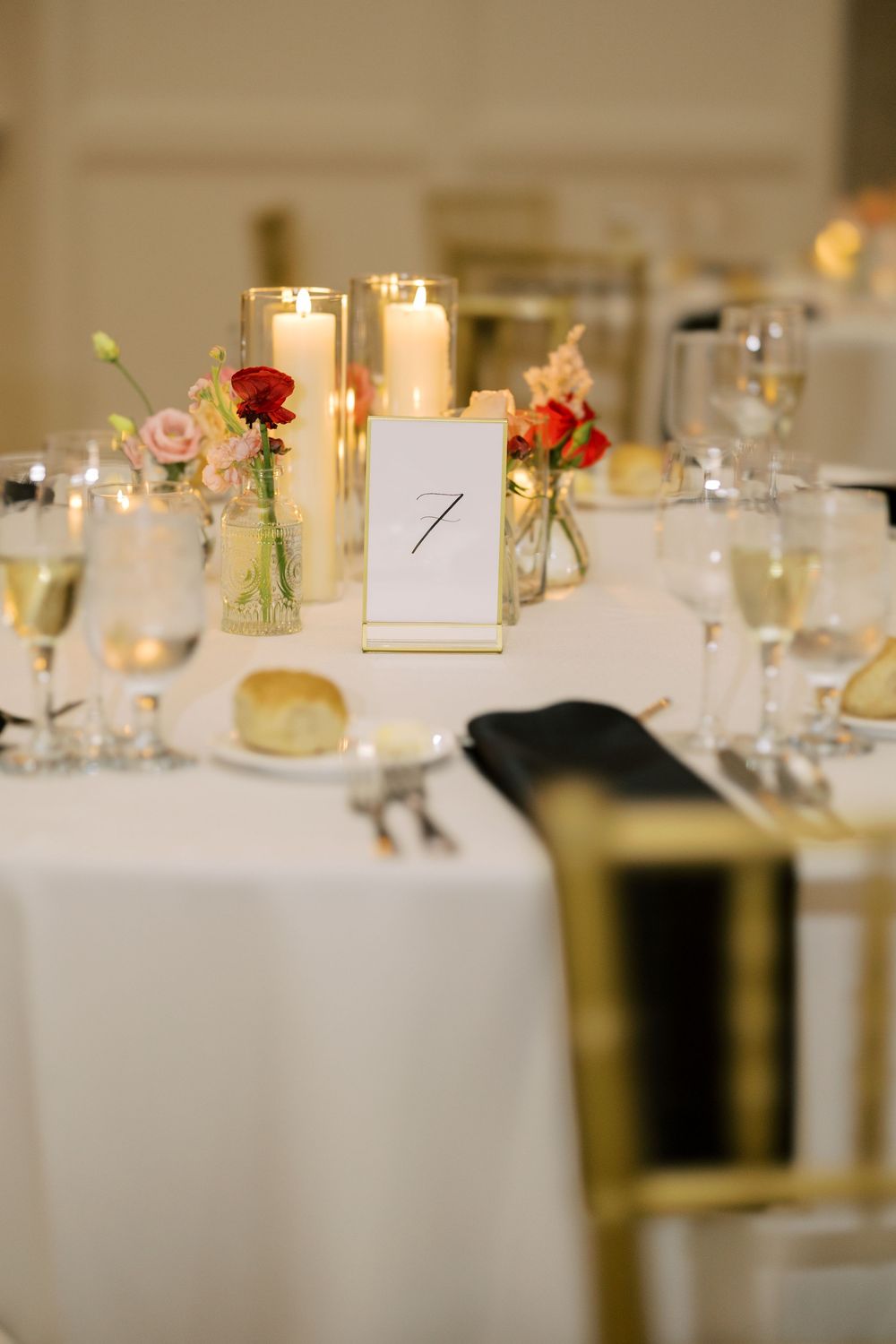Elegant wedding reception table setting with table number, lit candles, and small floral arrangements on white linens at Hall of Springs.