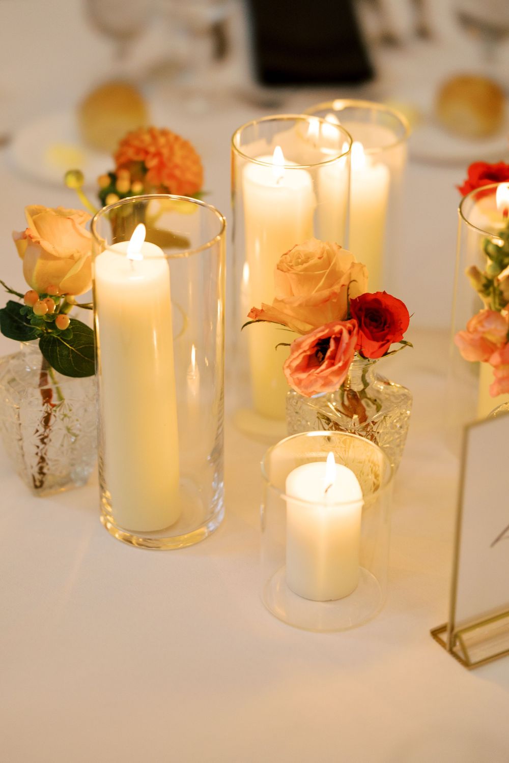 Elegant table setting with white pillar candles in glass holders and peach-colored roses creating a romantic atmosphere at Hall of Springs.