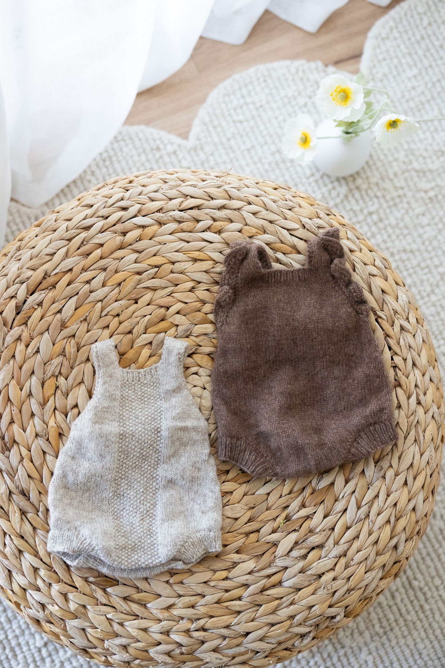Knitted baby bonnets and soft hats in neutral beige, pink, and white colors displayed on a woven rattan placemat.
