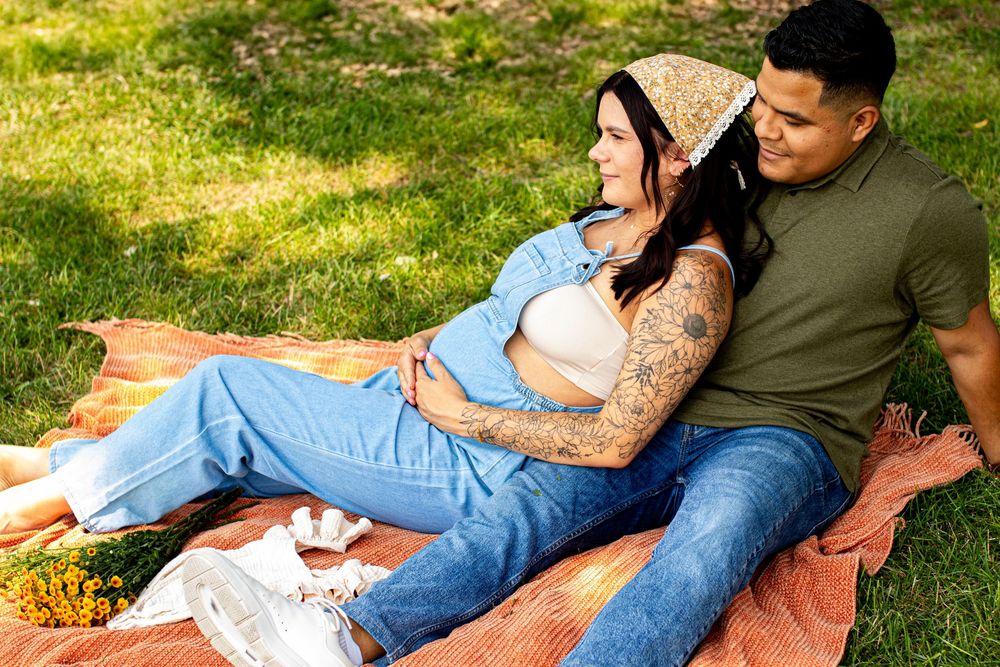 A couple relaxing on a blanket in a sunny field during a casual photoshoot.