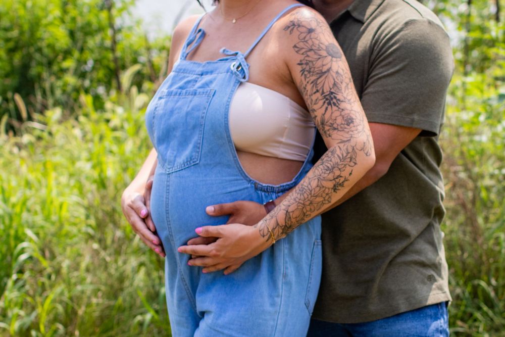 Couple embracing in an outdoor setting with one wearing denim overalls and the other in olive green.
