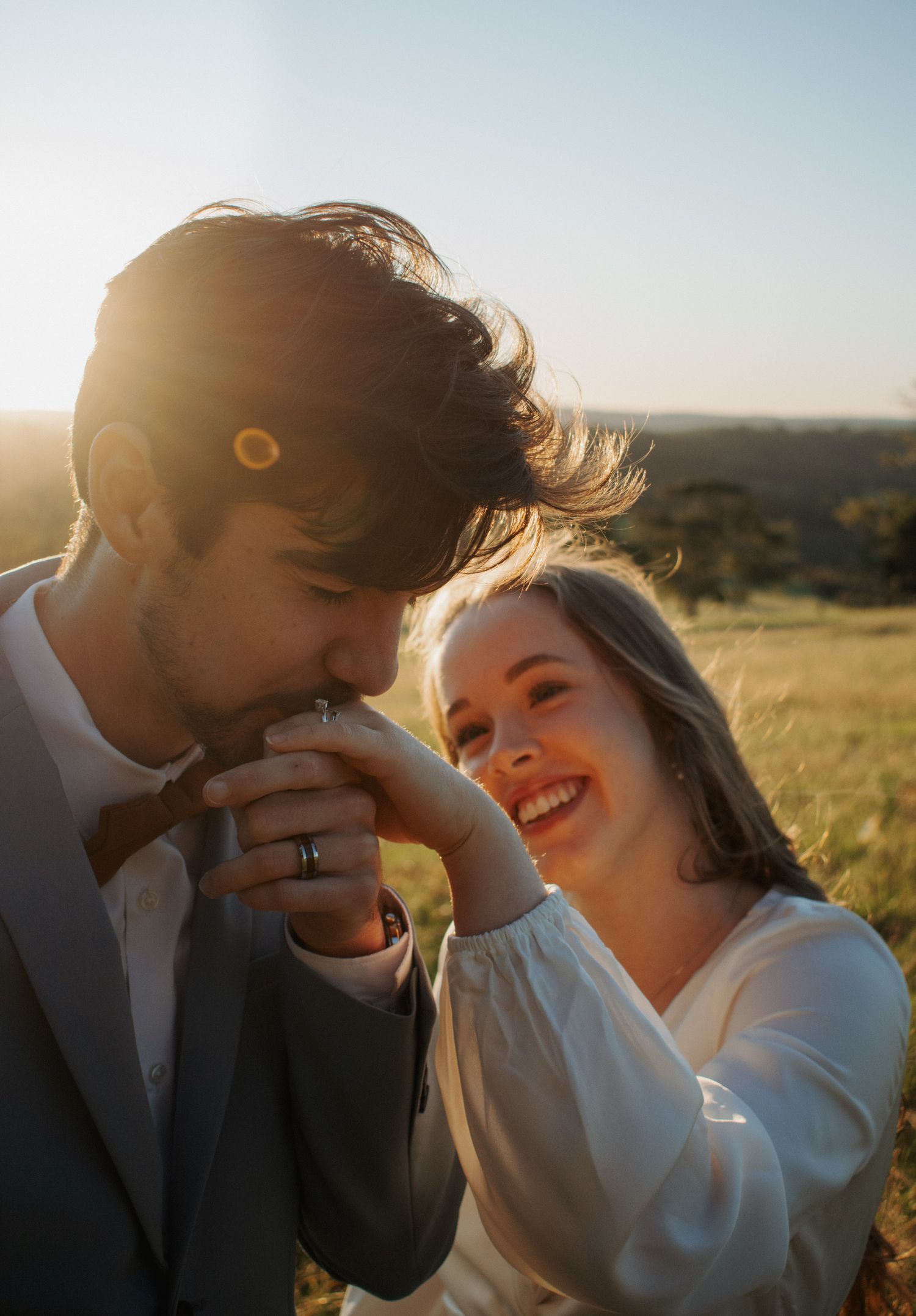 A joyful romantic moment between a couple in wedding attire at sunset in a grassy field.