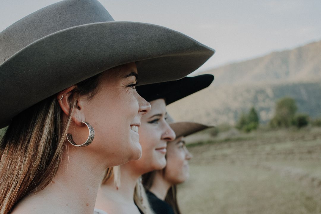 Three people wearing western hats standing together in profile against a mountainous desert landscape.