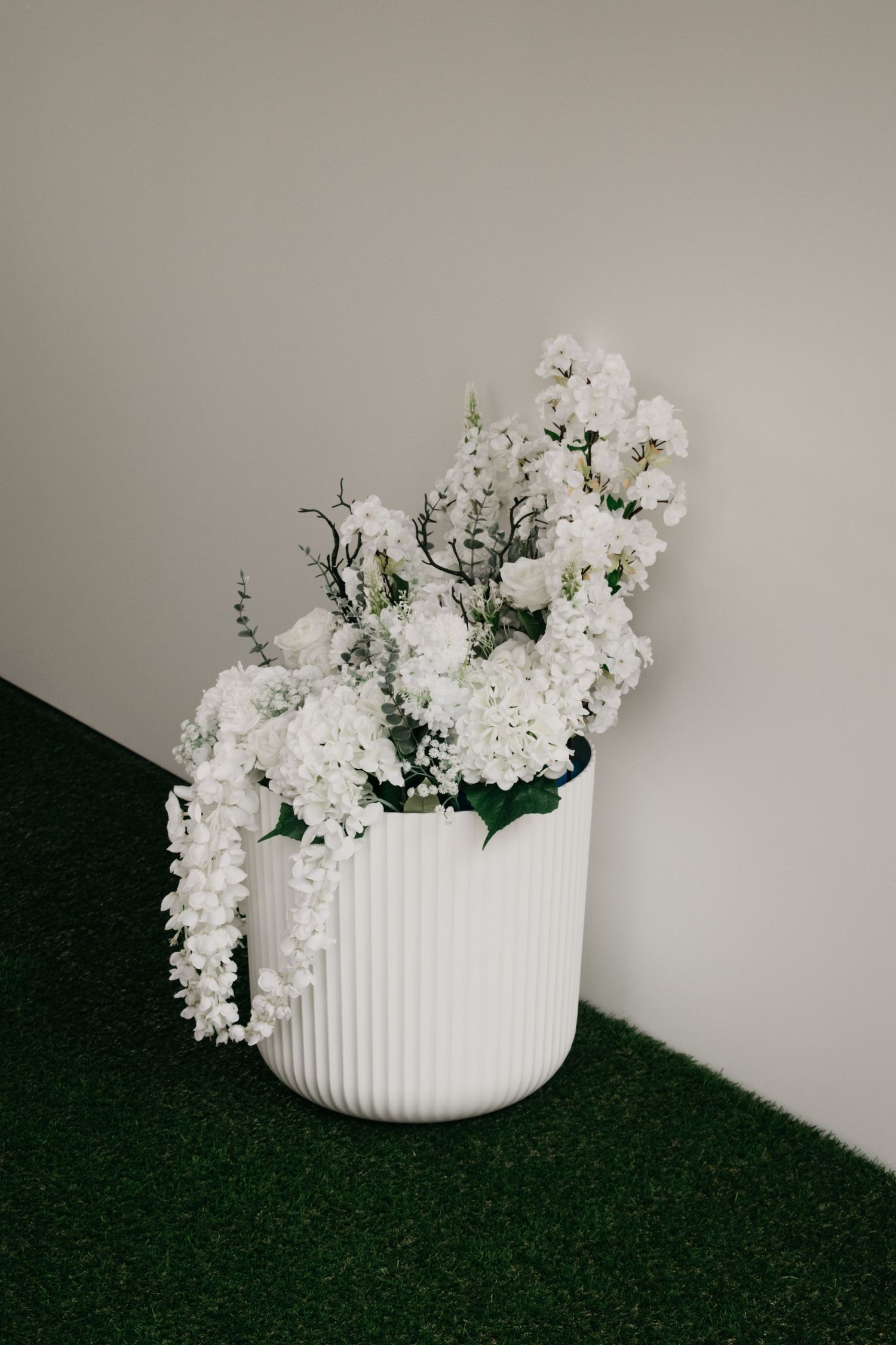 White ceramic vase filled with delicate white flowers sits elegantly against a neutral grey background.
