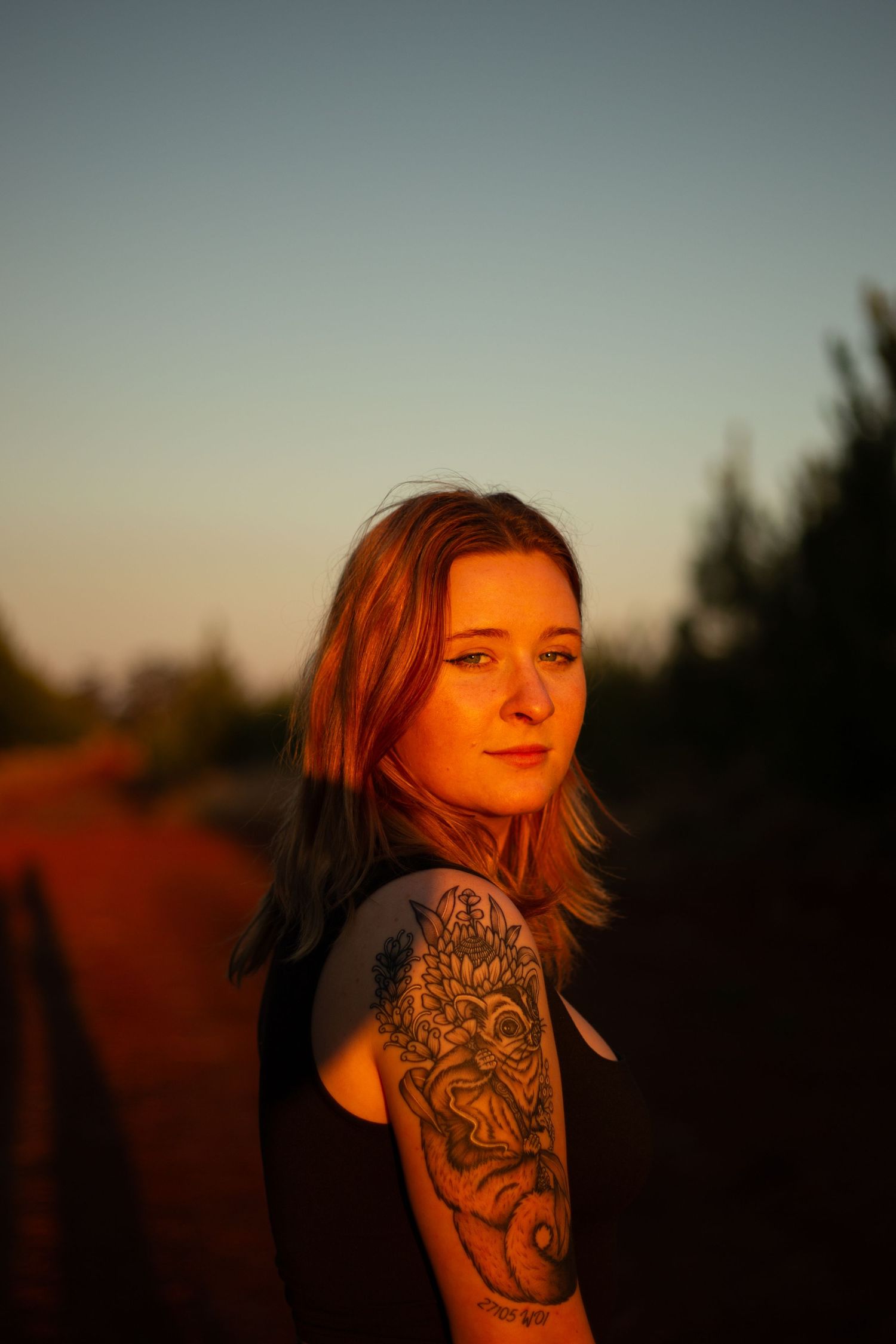 A person with an artistic arm tattoo stands silhouetted against a dusky orange sky.