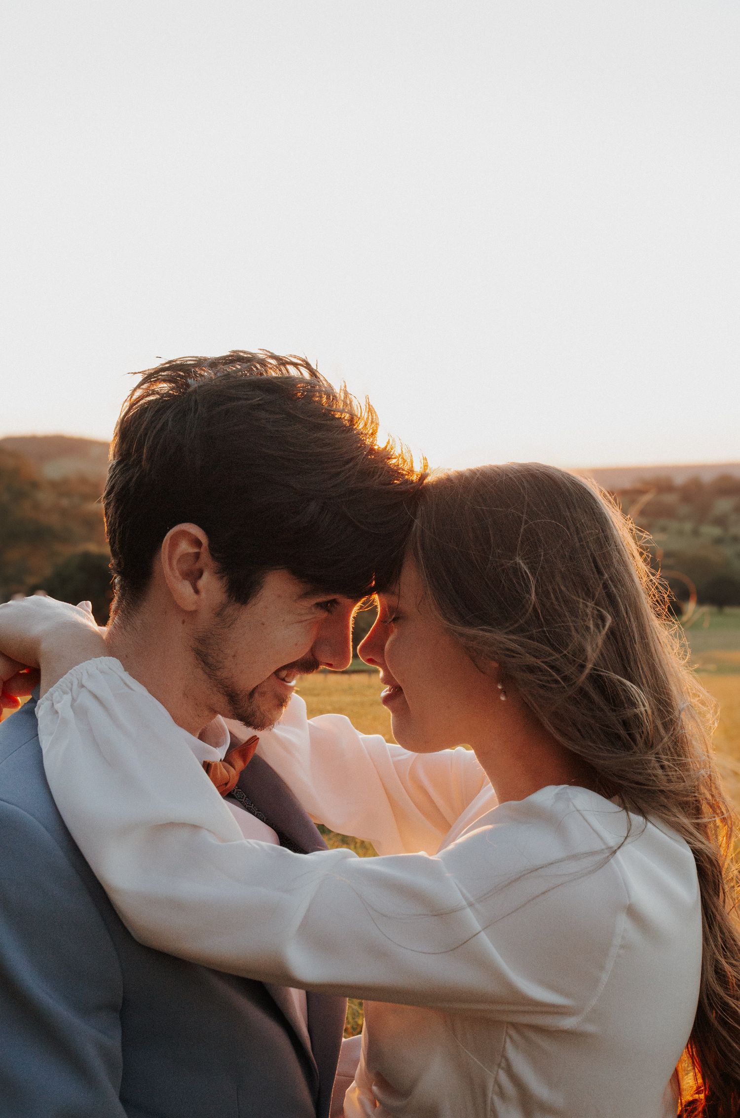 Romantic couple embracing during golden hour sunset with warm backlighting in an outdoor field.