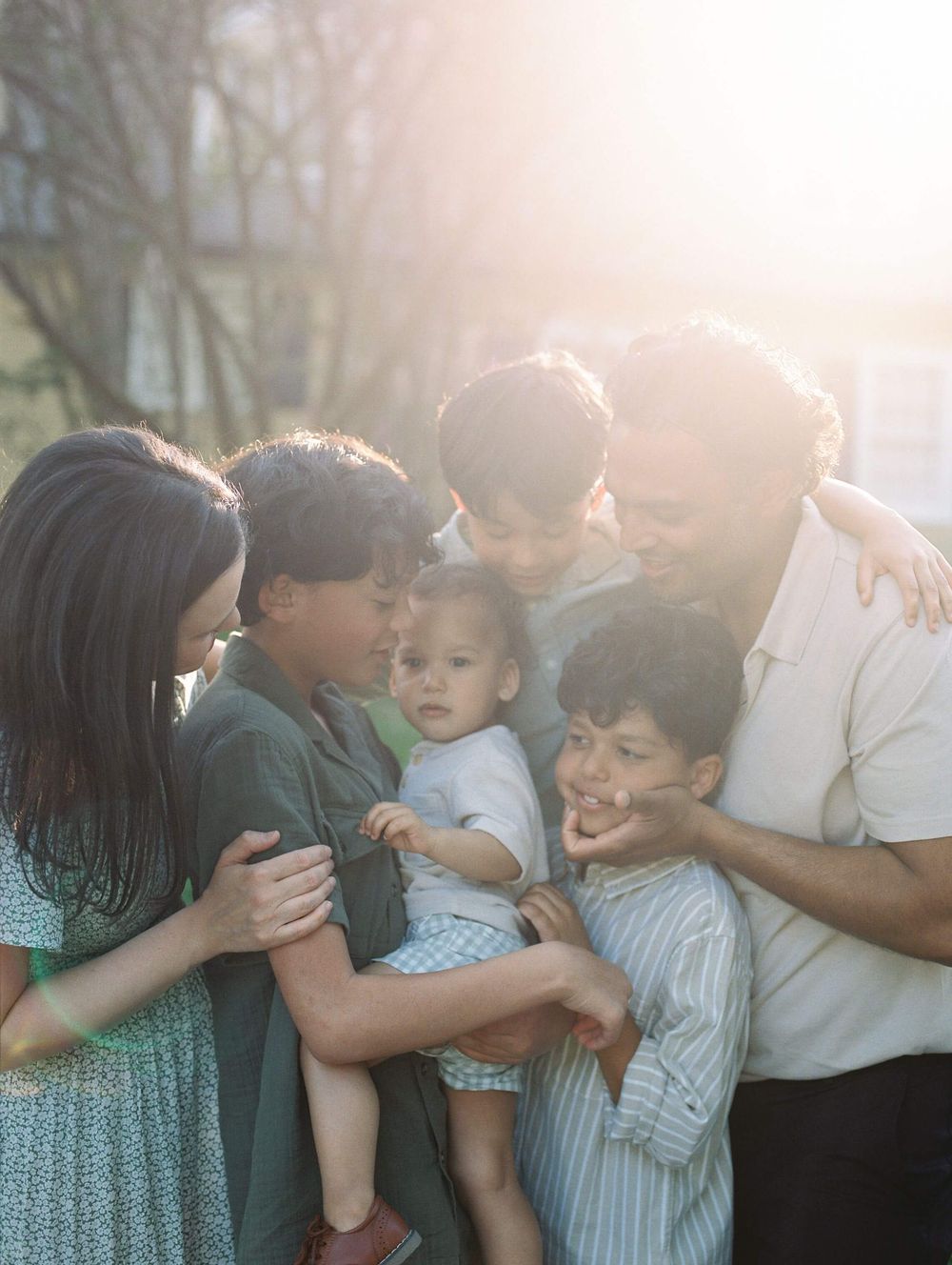 A loving family shares joyful embraces and laughter together in warm sunlit outdoor setting.