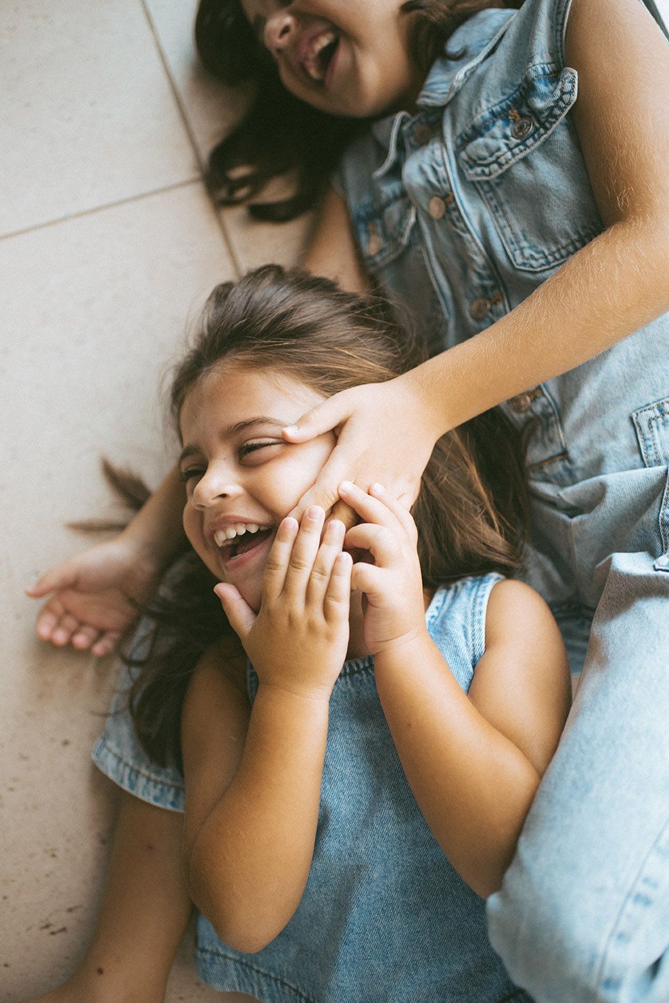 Two people in denim lying on the floor laughing and playing together in a candid joyful moment.