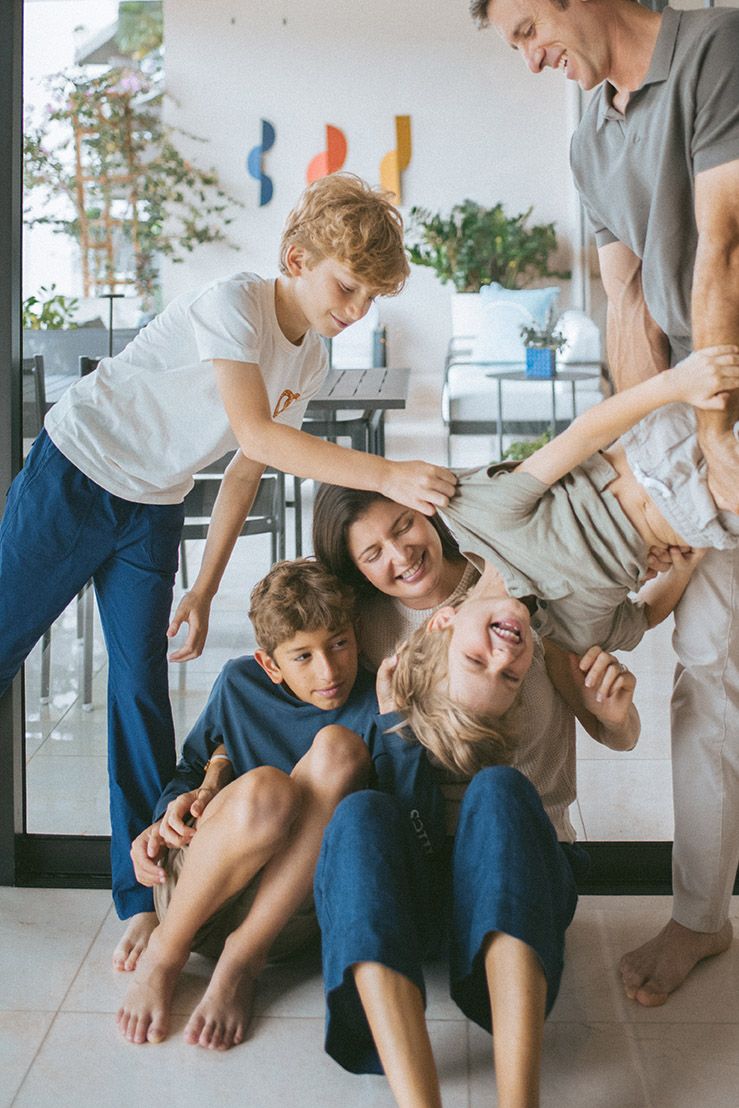A playful family scene with everyone laughing and being silly together on the floor in a bright room.