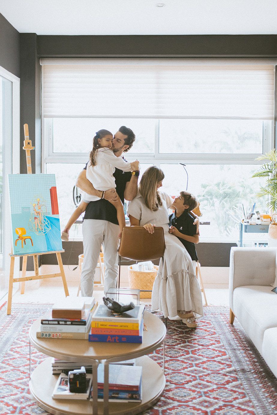 A warm family moment in a modern living room with an easel and books visible in the background.
