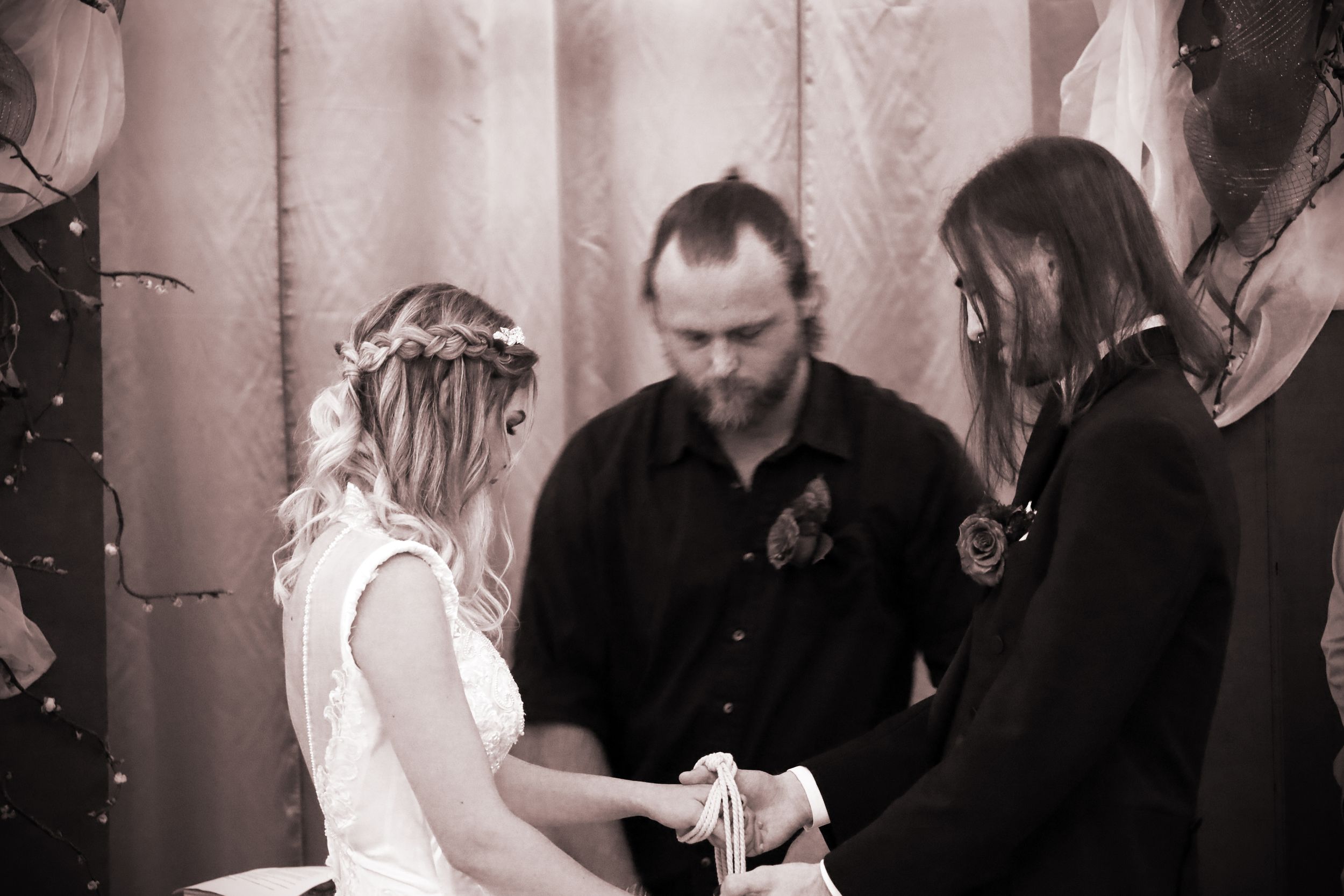 Bride and groom exchange vows during an intimate wedding ceremony with an officiant in black and white photo.