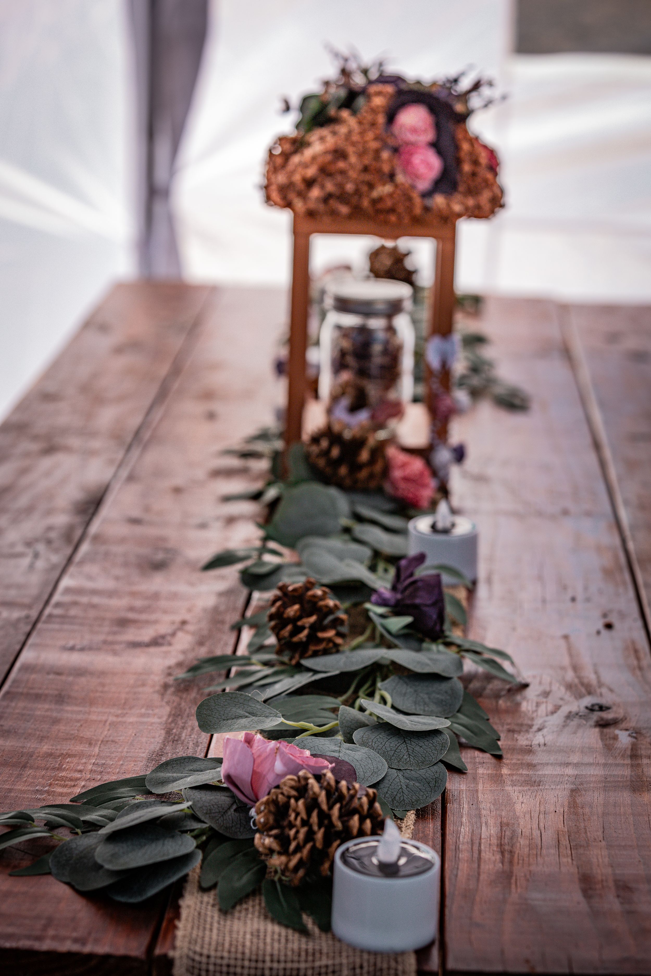 Rustic wooden table decorated with eucalyptus garland, pinecones, candles, and floral centerpiece.