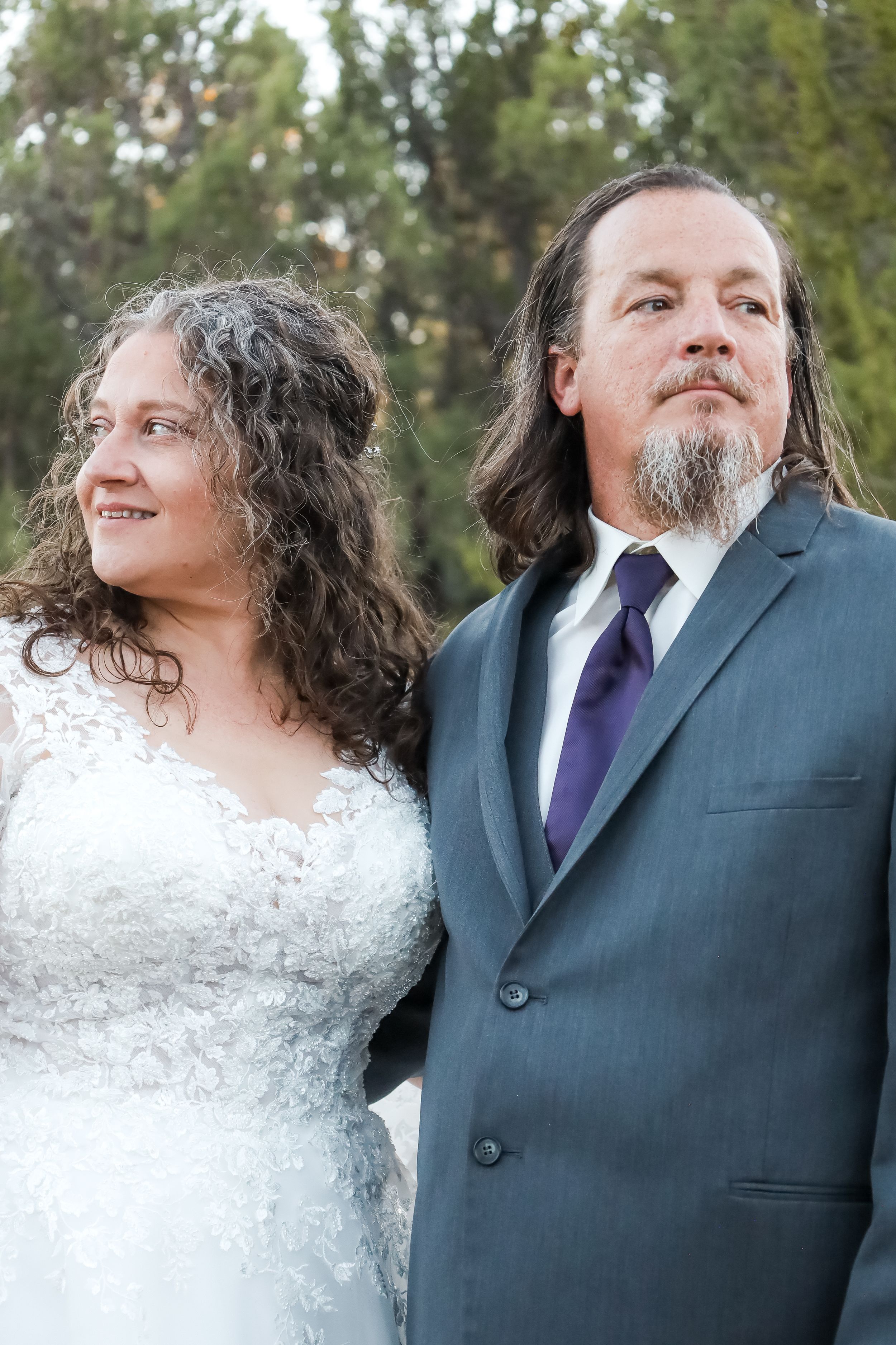 Bride and groom in gray suit with purple tie posing together outdoors during wedding portrait session.