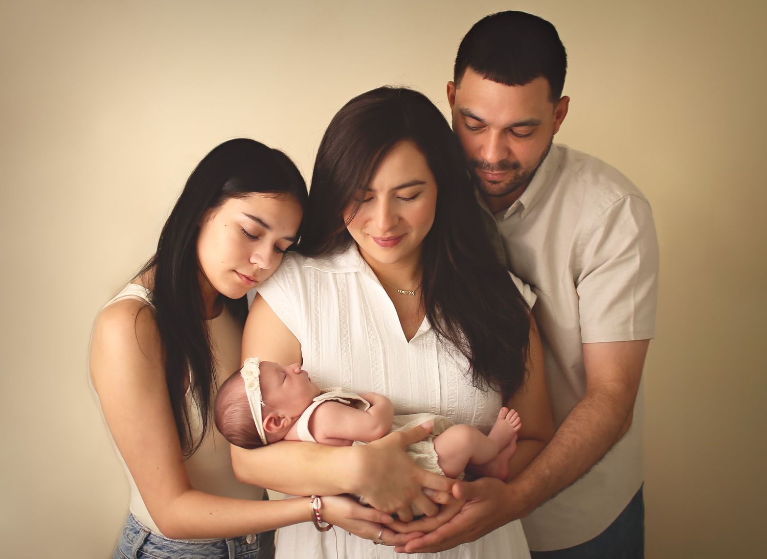 Mom, dad and big sister holding newborn baby sister in their arms for a posed photo as they look at her