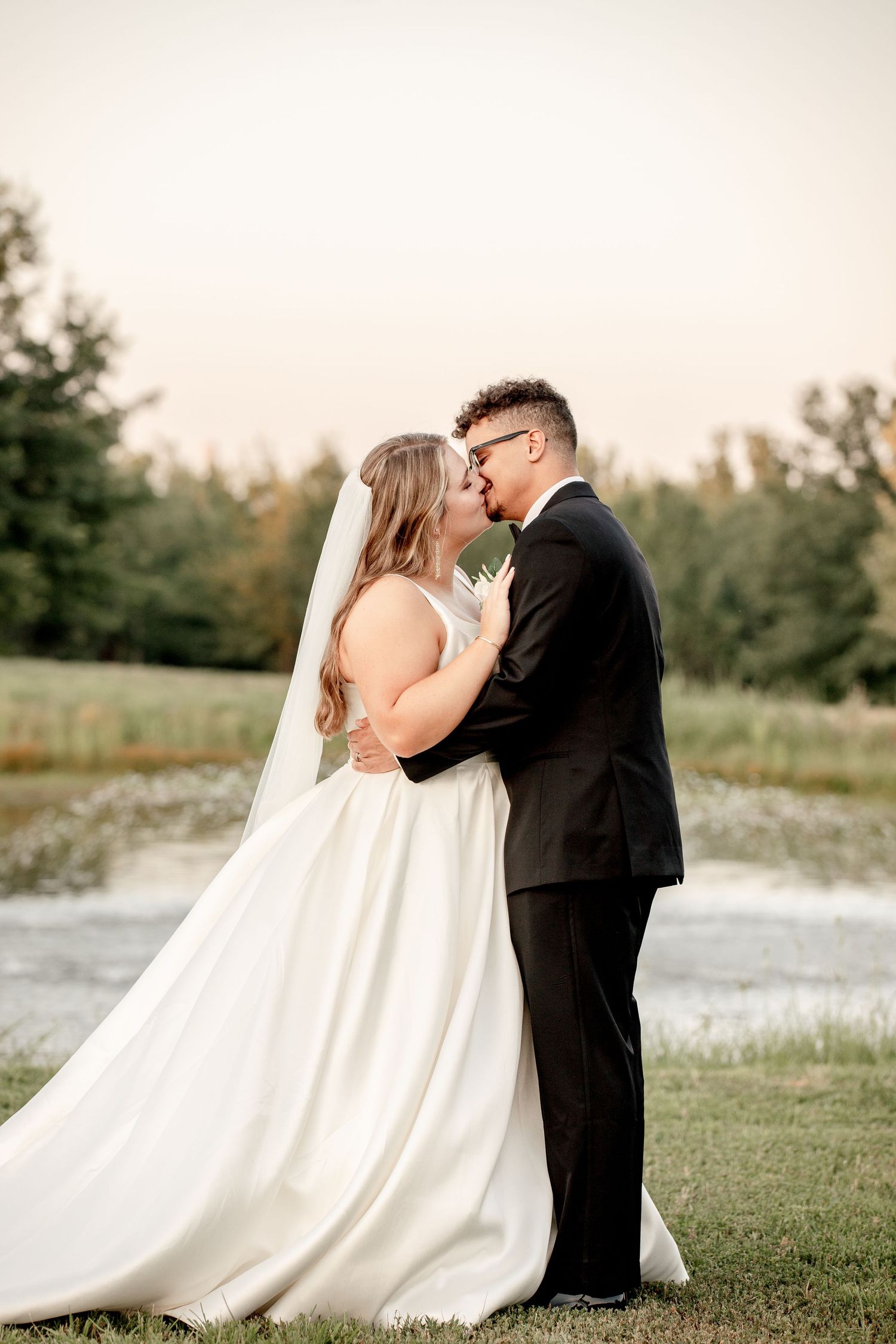 A couple embraces on a serene beach with turquoise water, the bride in a flowing gown holds a white bouquet.