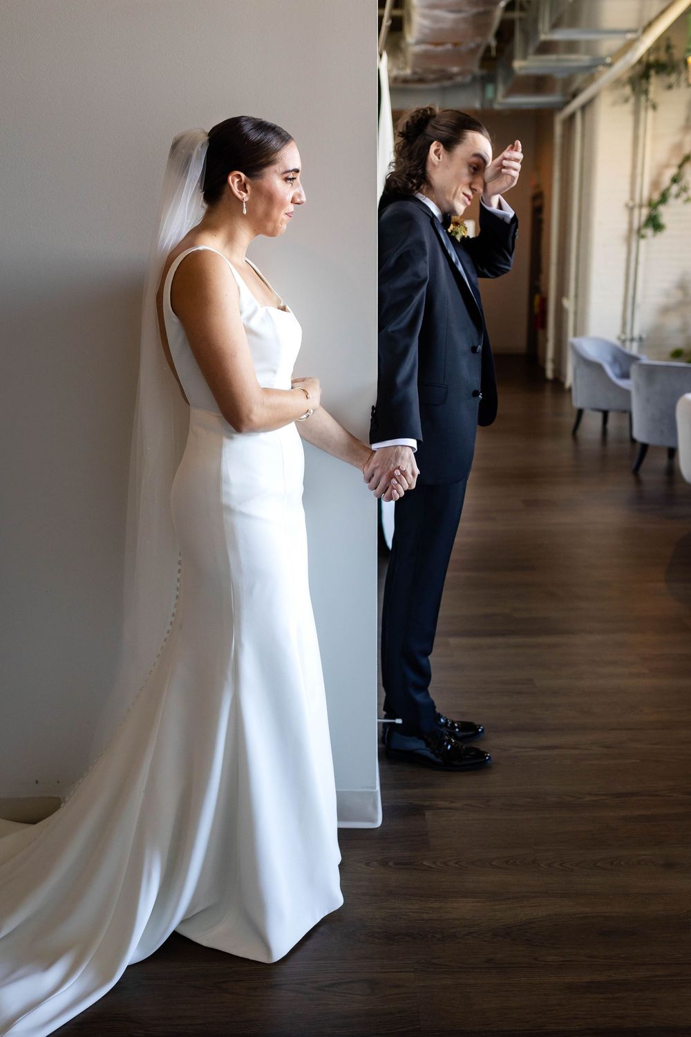 A bride and her partner share an emotional first look moment while holding hands on their wedding day.