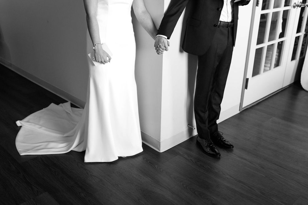 Black and white image showing the bottom half of a couple in wedding attire holding hands.
