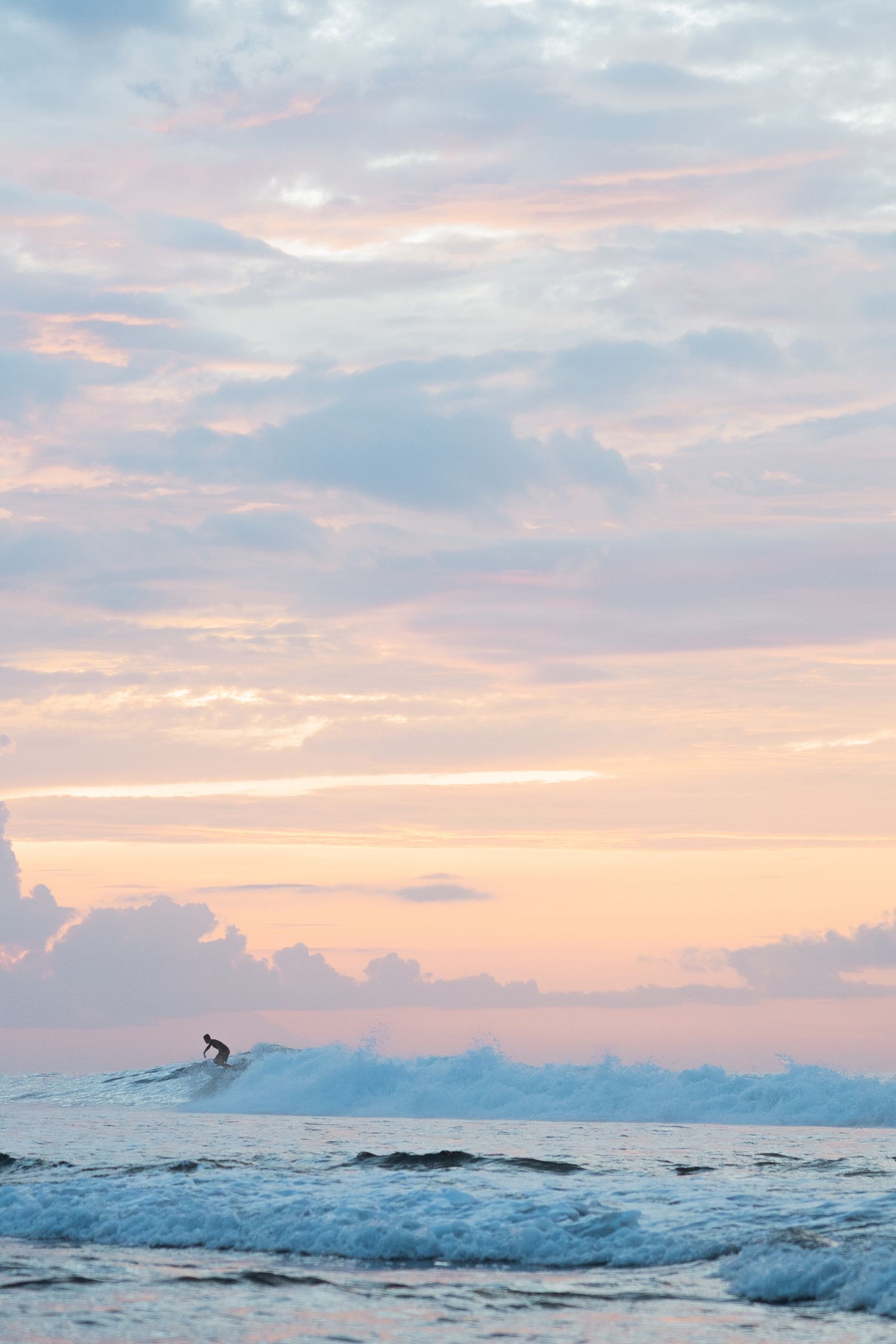 Serene sunset over ocean waves with a surfer silhouette in the distance.