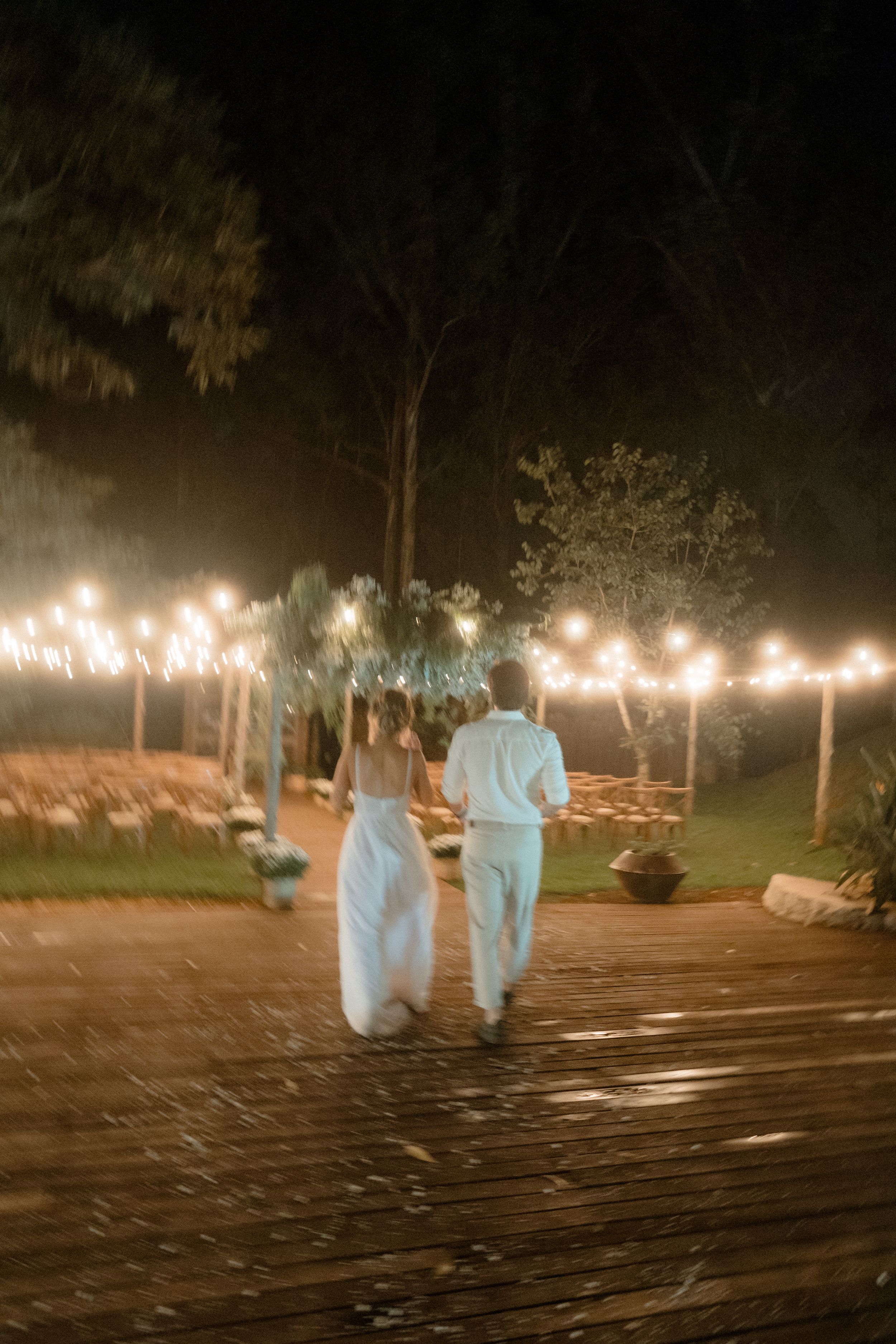 Couple walking on wooden deck illuminated by string lights in evening setting.