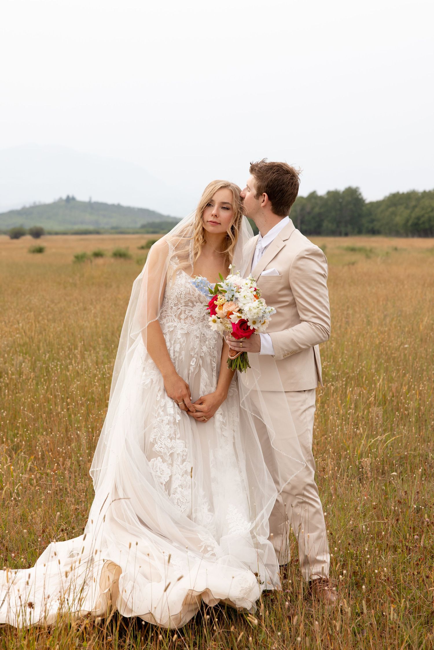 A couple shares a romantic moment in a golden field with mountains in the background during their wedding day.