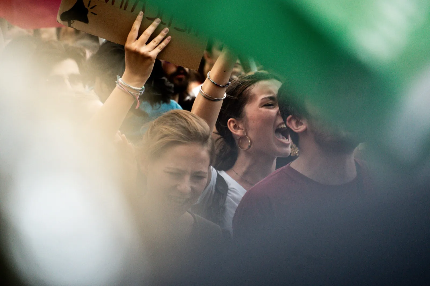 Visages de jeunes manifestants au milieu d’une foule serrée, tenant des pancartes sous une lumière rasante.