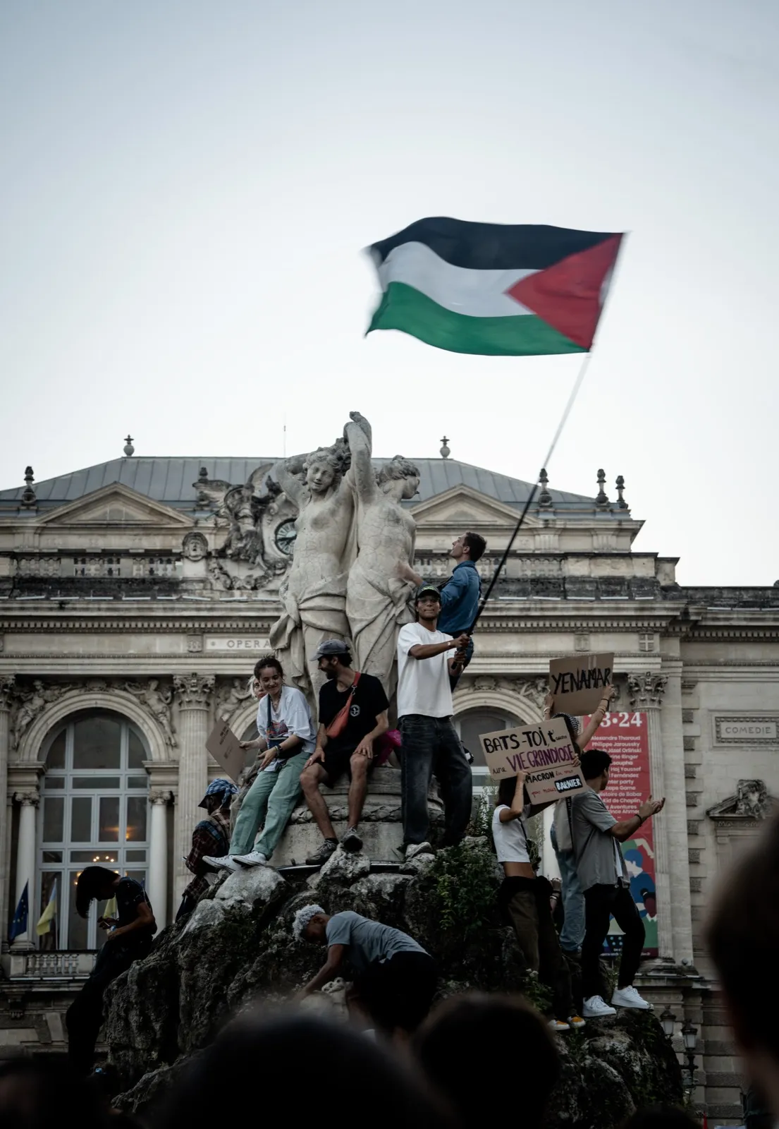 Manifestants rassemblés au pied d’une statue monumentale, brandissant un drapeau palestinien au sommet.