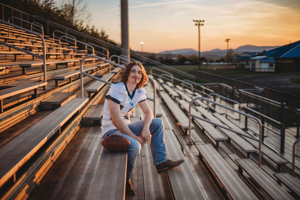 Person sitting on metal bleachers at sunset overlooking an empty sports field.