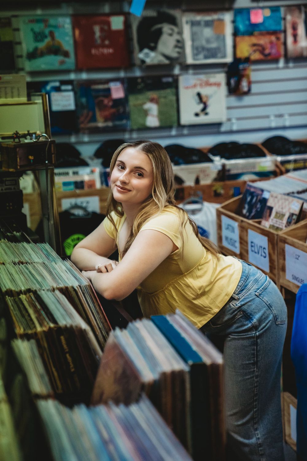 Person in yellow shirt browsing through vinyl records at a local music shop.