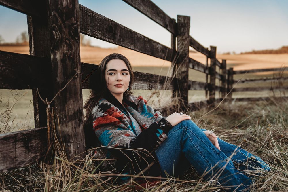 A rustic wooden fence stretches across rolling countryside hills during golden hour lighting.