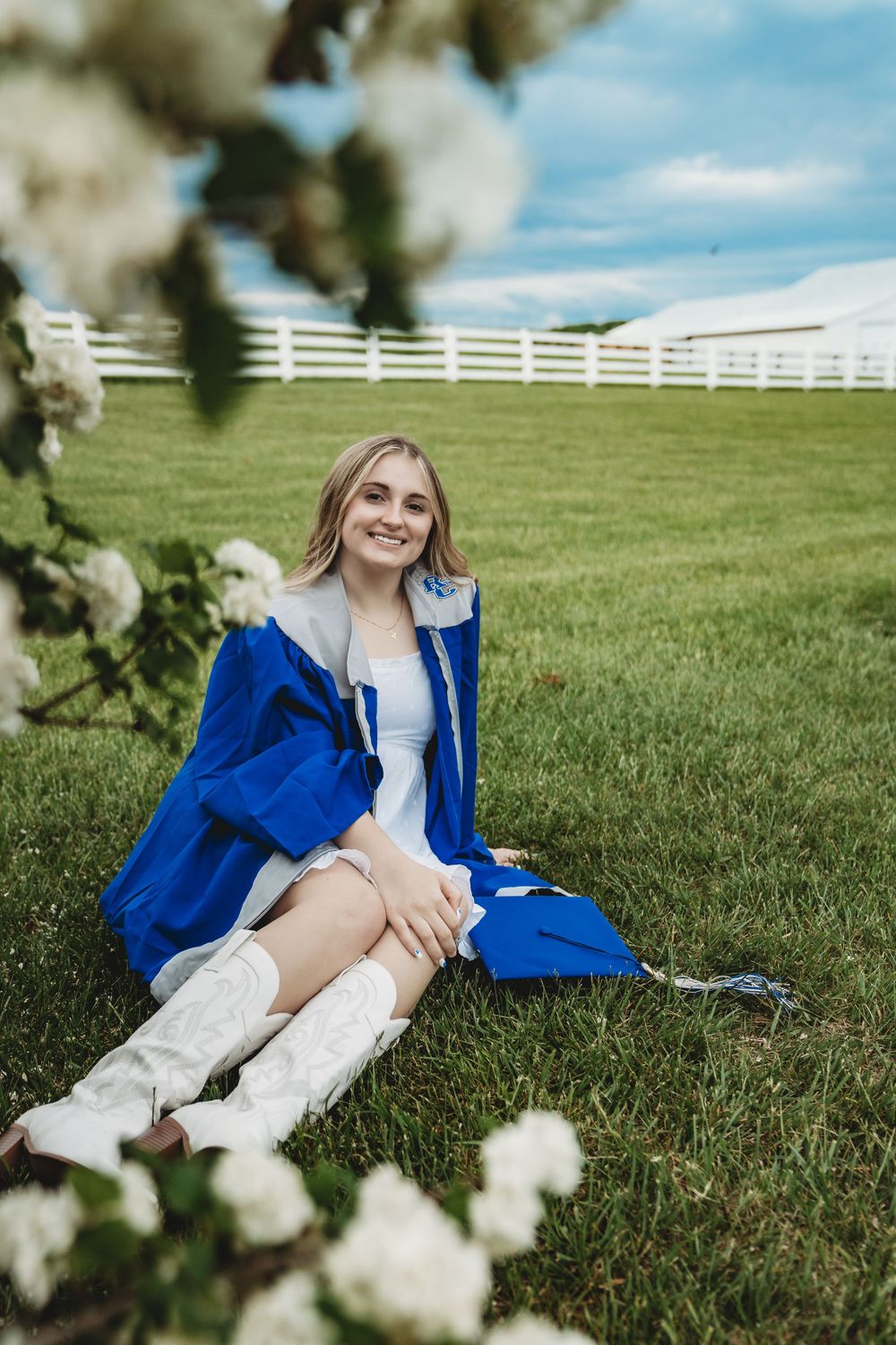 Senior photos in green field with white fence and spring blossoms.