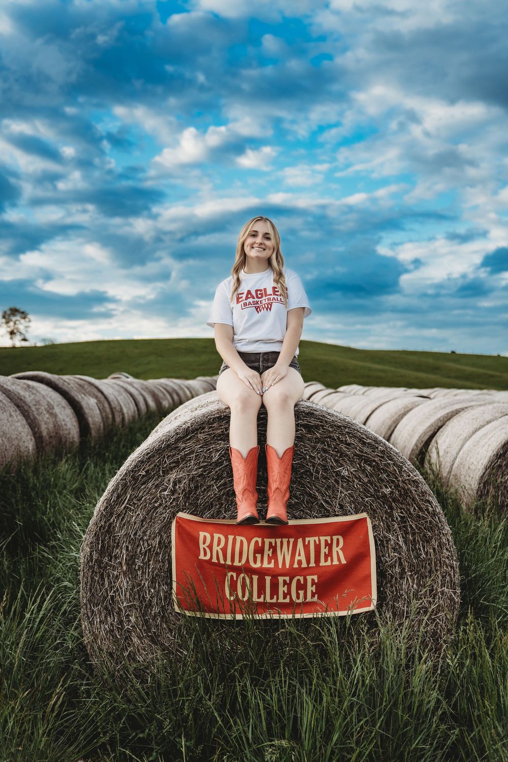 Creative senior portrait on hay bales with Bridgewater College banner.